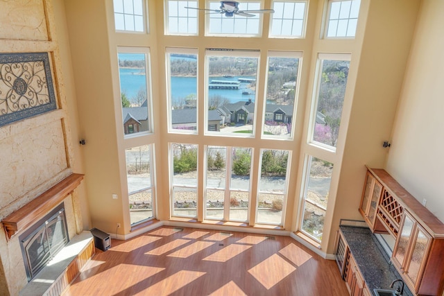 living room featuring a water view, a towering ceiling, a glass covered fireplace, and light wood-style floors