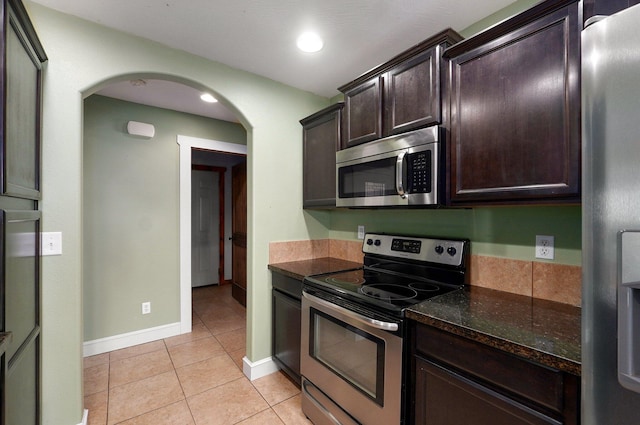 1471 Woodland Rd, Marshfield, MO 65706 - kitchen with appliances with stainless steel finishes, arched walkways, light tile patterned floors, dark brown cabinetry, and dark stone countertops