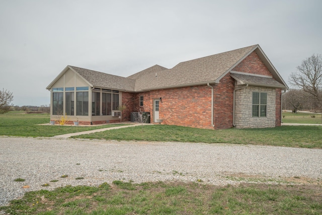 rear view of property featuring a sunroom, brick siding, roof with shingles, driveway, and a yard