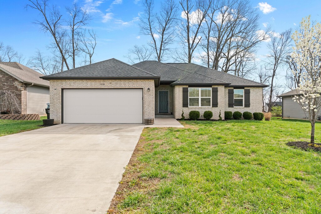 ranch-style home with a front lawn, an attached garage, brick siding, and concrete driveway