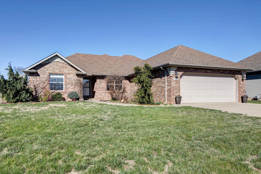 ranch-style home with roof with shingles, an attached garage, driveway, a front yard, and brick siding