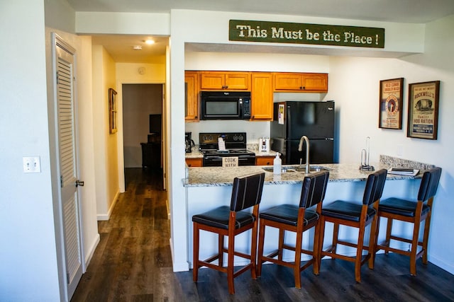 kitchen featuring a peninsula, brown cabinetry, black appliances, and dark wood finished floors