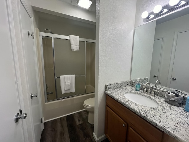 bathroom featuring toilet, bath / shower combo with glass door, wood finished floors, and vanity