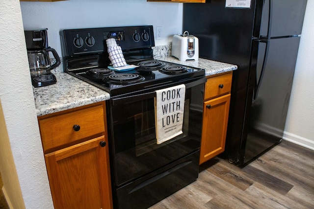 kitchen featuring brown cabinets, black appliances, light stone countertops, and dark wood-type flooring