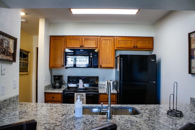 kitchen featuring black appliances, light stone countertops, and a sink