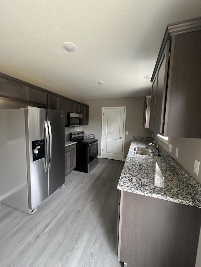 kitchen with stainless steel appliances, a sink, light stone counters, dark brown cabinets, and wood finished floors