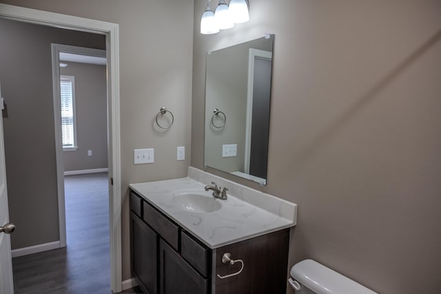 half bathroom with baseboards, wood finished floors, toilet, and vanity