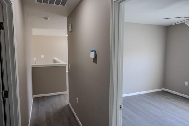 hall with baseboards, visible vents, an upstairs landing, and wood finished floors
