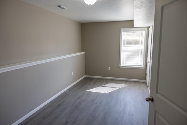 empty room with wood finished floors, baseboards, and visible vents