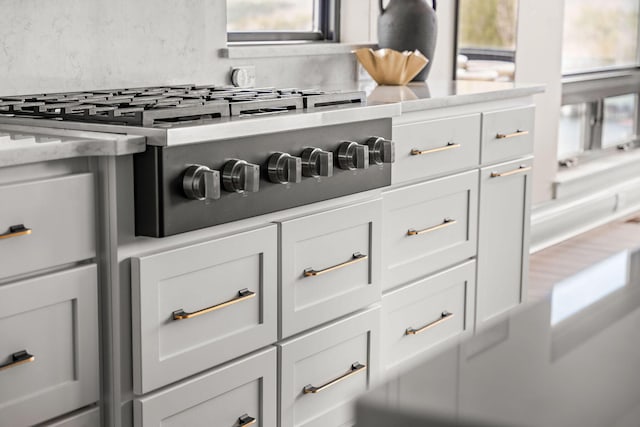 interior details featuring white cabinets, stainless steel gas stovetop, light stone counters, and decorative backsplash