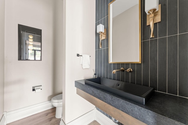 half bathroom with toilet, a sink, baseboards, and wood finished floors