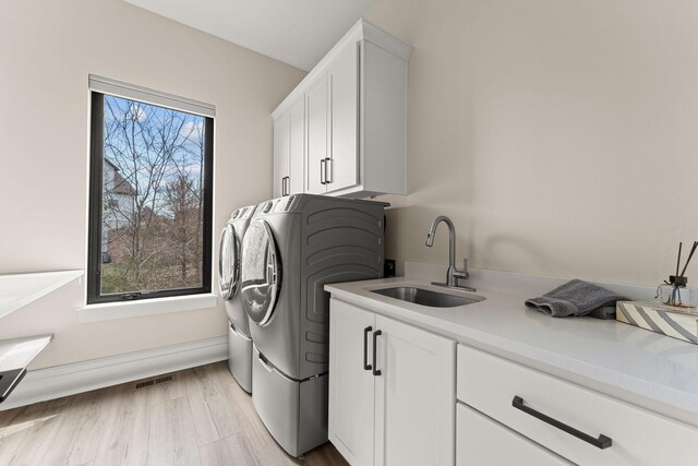 washroom with a wealth of natural light, washing machine and clothes dryer, cabinet space, and a sink