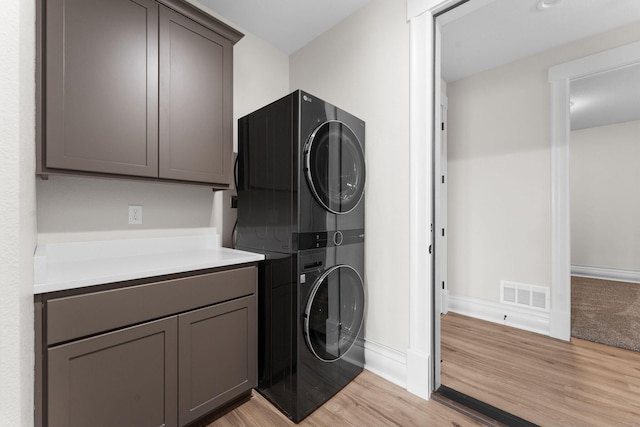 washroom featuring visible vents, light wood finished floors, baseboards, stacked washer and dryer, and cabinet space