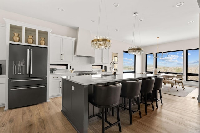 kitchen with decorative backsplash, high end fridge, a sink, custom range hood, and an inviting chandelier