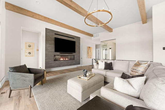 living room featuring a notable chandelier, beam ceiling, a large fireplace, visible vents, and light wood-style floors