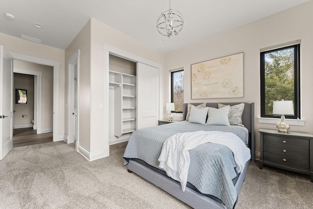carpeted bedroom featuring a closet, baseboards, and a notable chandelier
