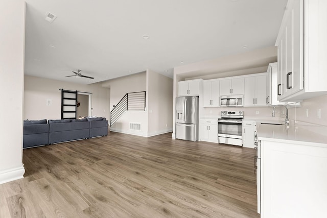 kitchen featuring light countertops, light wood finished floors, appliances with stainless steel finishes, white cabinetry, and open floor plan