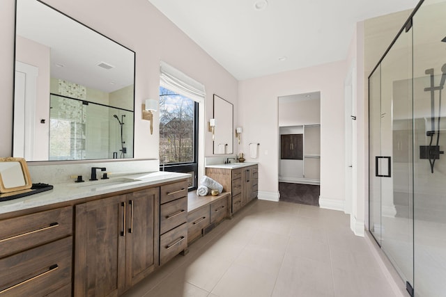 bathroom with a stall shower, tile patterned floors, a sink, two vanities, and baseboards