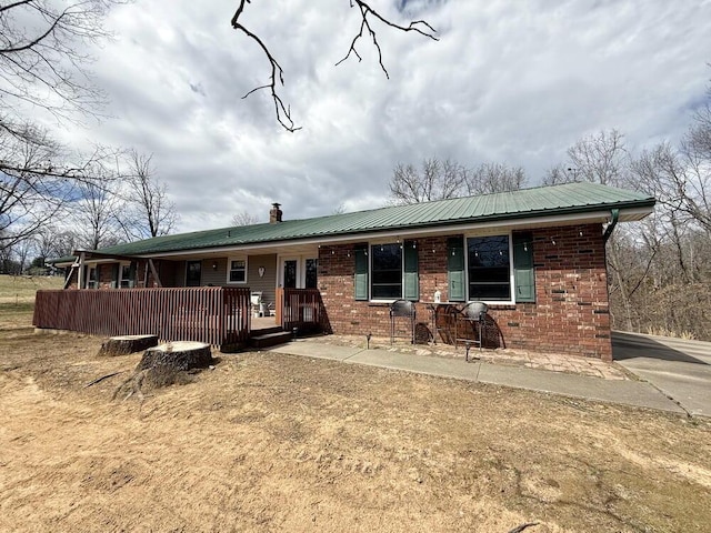 ranch-style house featuring metal roof, a chimney, and brick siding