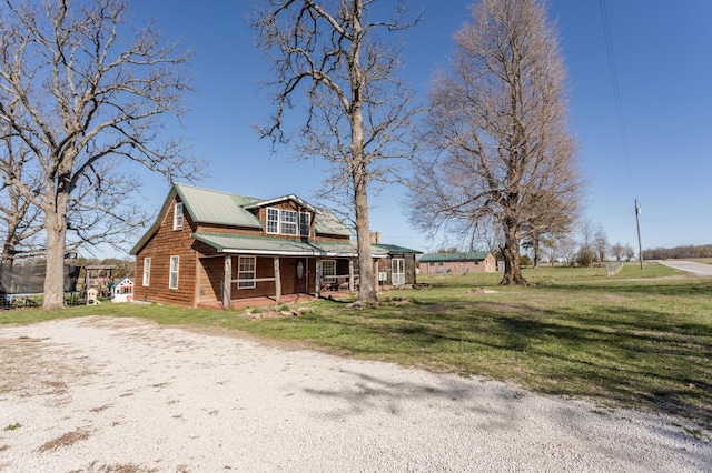 view of front facade with a front yard, covered porch, a trampoline, metal roof, and dirt driveway