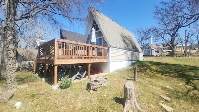 view of home's exterior with a storage shed, a deck, roof with shingles, a lawn, and an outbuilding