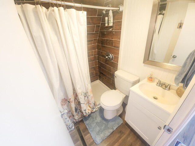 bathroom featuring toilet, wood finished floors, tiled shower, and vanity