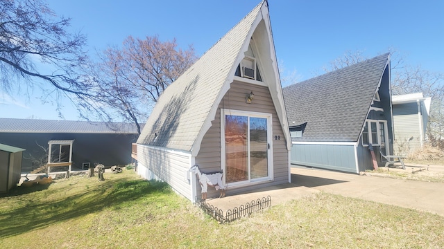 back of house with a lawn, an outbuilding, and roof with shingles