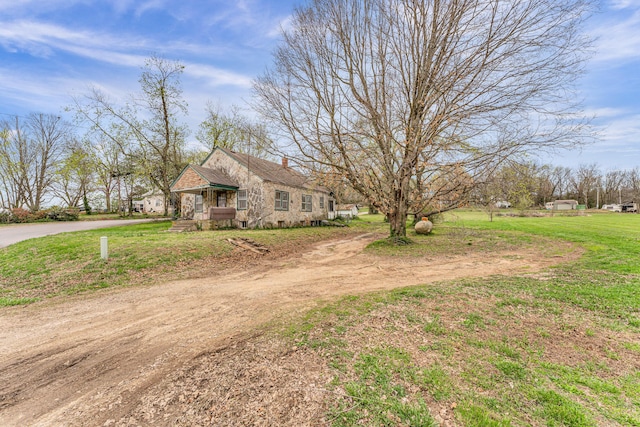 view of front of home featuring driveway, a chimney, stone siding, and a front yard
