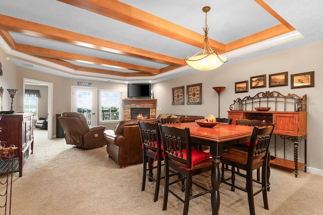 dining room featuring a tray ceiling, a fireplace, baseboards, light colored carpet, and visible vents