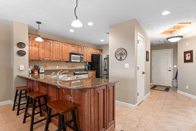 kitchen featuring a peninsula, brown cabinets, tasteful backsplash, appliances with stainless steel finishes, and a sink