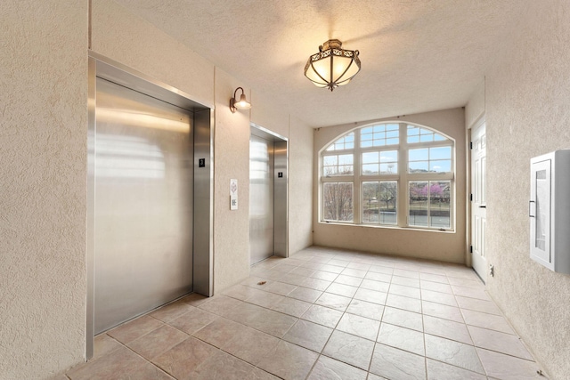 hallway with elevator, a textured wall, and tile patterned floors