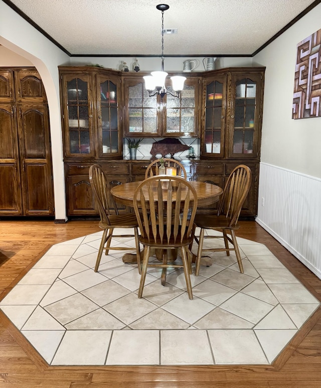 dining space with a textured ceiling, crown molding, a notable chandelier, and wainscoting