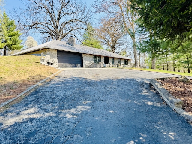 view of home's exterior featuring driveway, stone siding, an attached garage, and a chimney