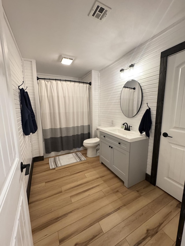 bathroom with vanity, toilet, a shower with shower curtain, visible vents, and wood finished floors