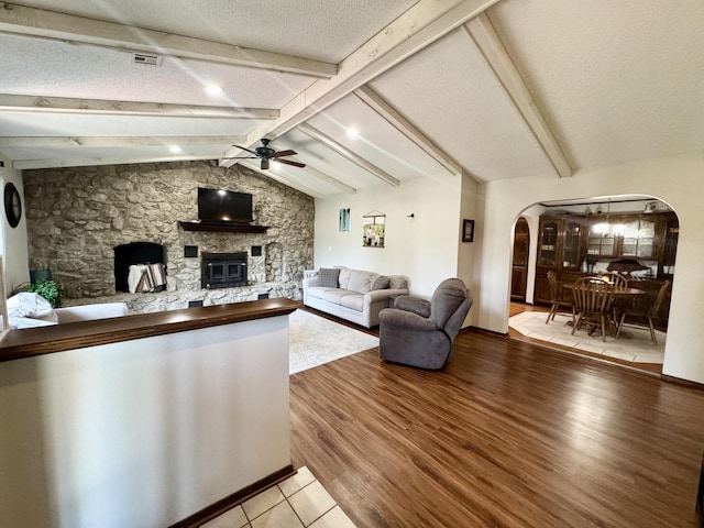 living room featuring a textured ceiling, arched walkways, ceiling fan, vaulted ceiling with beams, and a fireplace