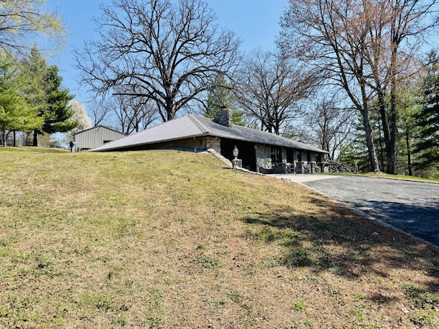 view of side of property with aphalt driveway, a yard, and a chimney