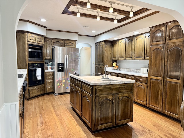 kitchen featuring light countertops, light wood-style flooring, arched walkways, a sink, and black appliances