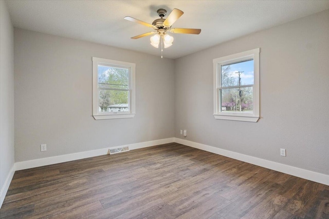 empty room with baseboards, dark wood-style floors, visible vents, and plenty of natural light