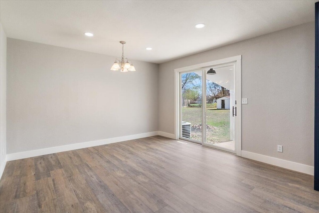 unfurnished room featuring baseboards, wood finished floors, an inviting chandelier, and recessed lighting