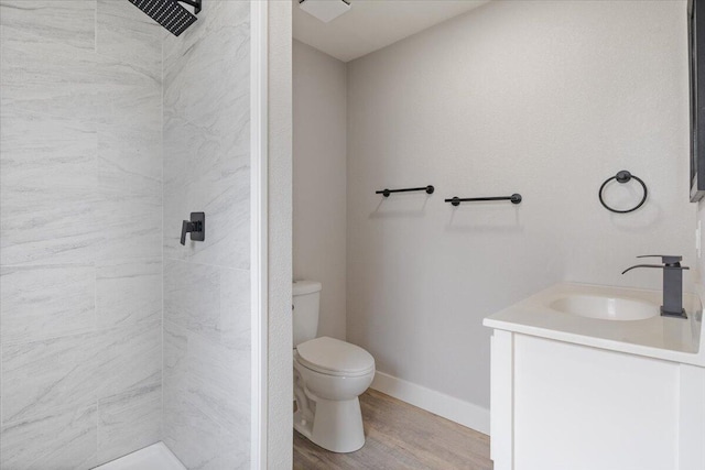 bathroom with baseboards, a tile shower, toilet, wood finished floors, and vanity