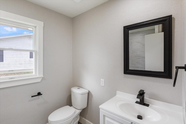 half bathroom featuring toilet, a healthy amount of sunlight, and vanity