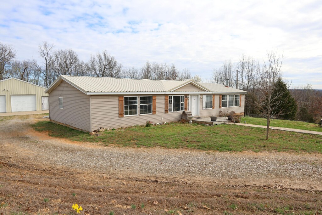 ranch-style home with an outbuilding, metal roof, a detached garage, a front lawn, and dirt driveway