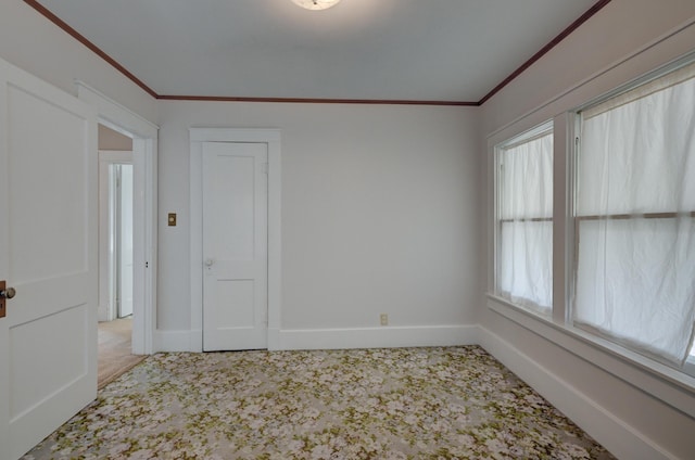 carpeted empty room featuring crown molding and baseboards