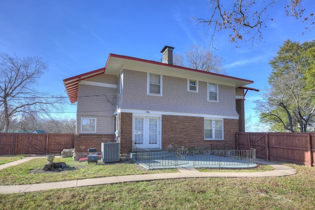 back of house featuring central AC unit, a chimney, a fenced backyard, and brick siding