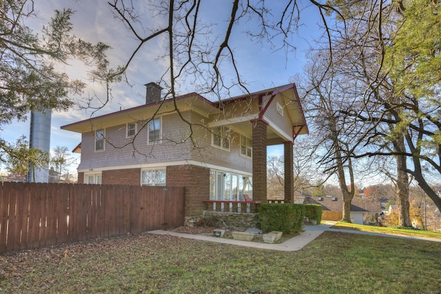 view of side of home featuring a chimney, fence, brick siding, and a yard