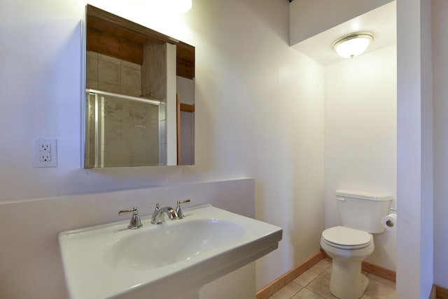 bathroom featuring toilet, a sink, a shower stall, tile patterned flooring, and baseboards