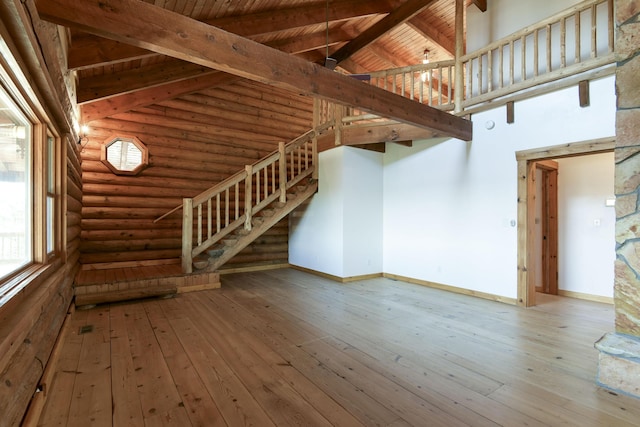 unfurnished living room with stairs, log walls, high vaulted ceiling, hardwood / wood-style flooring, and beamed ceiling