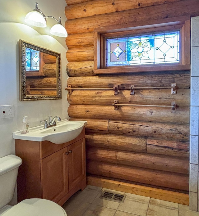 bathroom featuring visible vents, toilet, rustic walls, and vanity