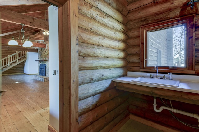 bathroom with a stone fireplace, log walls, a sink, and hardwood / wood-style flooring