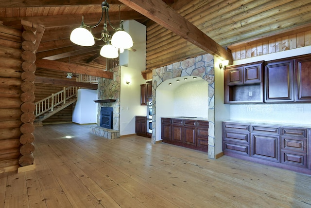 kitchen with light wood finished floors, beam ceiling, rustic walls, a stone fireplace, and double oven